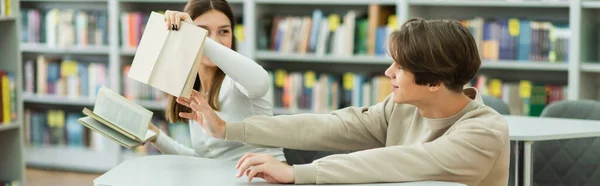 Teen girl holding books while sitting with friend in reading room, banner - foto de stock