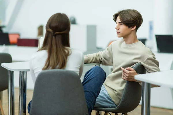 Student looking at blurred teen girl while sitting in reading room — Stock Photo