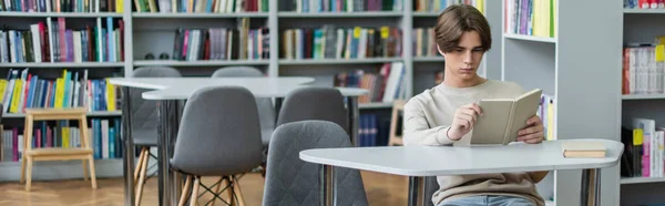 Teenage boy sitting in library reading room with book, banner — Stock Photo
