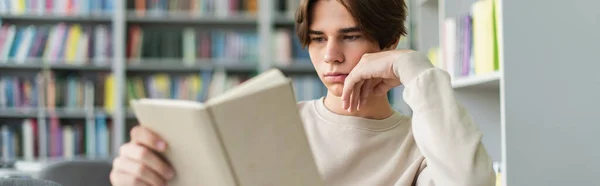 Concentrated student reading book in library on blurred background, banner — Photo de stock