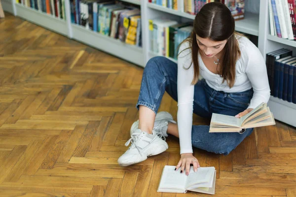 High angle view of teenage girl with books sitting on floor in library — Stock Photo