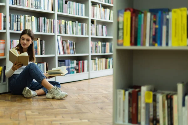 Тинейджер выбирает книги, сидя на полу в библиотеке — стоковое фото