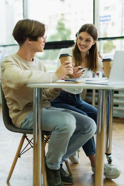 Happy teenage girl talking to friend near laptop in library reading room — Foto stock