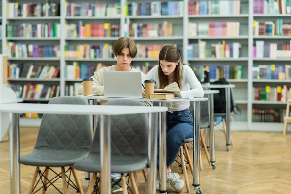 Teenage students studying near laptop and books in library - foto de stock