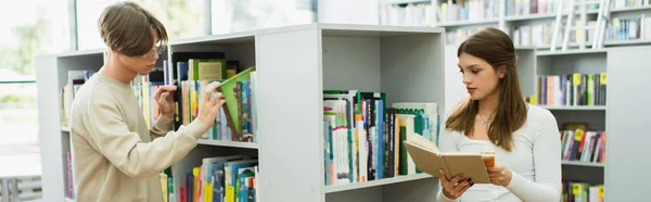 Подросток выбирает книги на полках рядом друг читает в библиотеке, баннер — стоковое фото