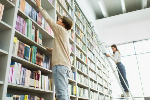 Low angle view of students choosing books from variety on racks in library — Foto stock