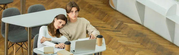 Teenage students looking at camera near books and laptop in library, banner — Stock Photo