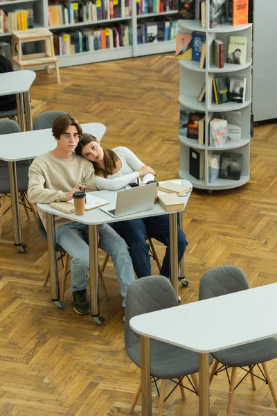 Teenage friends looking at camera while sitting near laptop in library reading room — Stock Photo