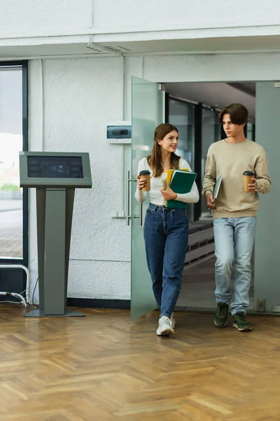 Teenage students with notebooks and laptop entering library — Stock Photo