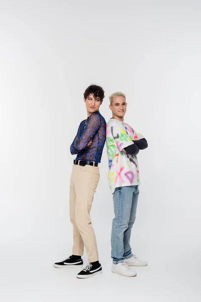 Full length of trendy gay man and queer person standing back to back with crossed arms on grey background — стоковое фото