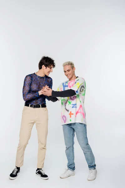 Full length of positive gay holding hands of stylish queer person on grey background — Stockfoto