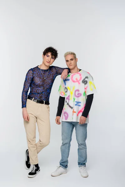 Stylish queer person leaning on gay man while looking at camera on grey background — Fotografia de Stock