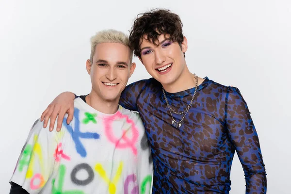 Happy nonbinary person embracing smiling gay man and looking at camera isolated on grey — стоковое фото