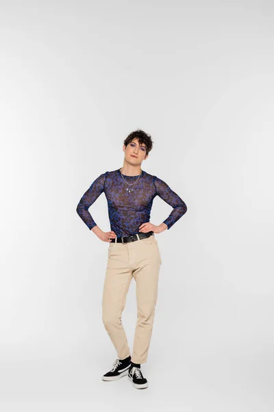 Full length of nonbinary model in beige trousers posing with hands on waist on grey background — Foto stock