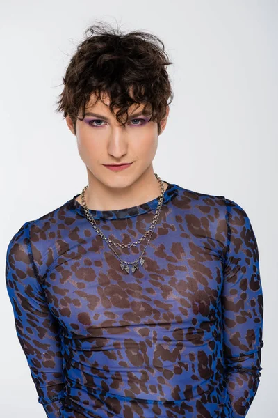 Brunette nonbinary model in long sleeve shirt and silver necklaces looking at camera isolated on grey — Foto stock