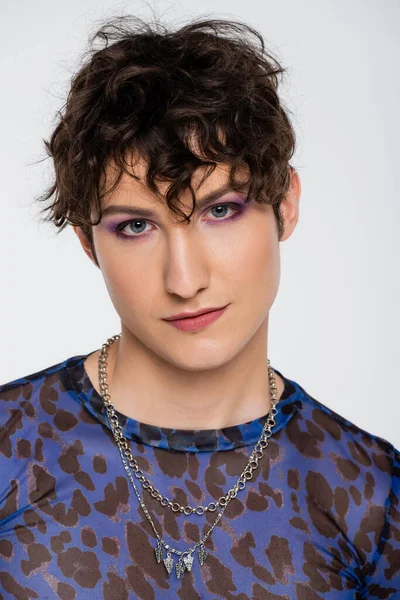 Portrait of brunette queer person with makeup looking at camera isolated on grey - foto de stock