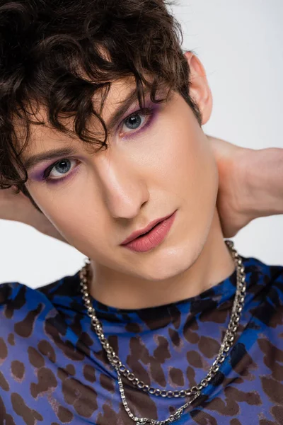 Close up portrait of young queer model with makeup looking at camera isolated on grey - foto de stock