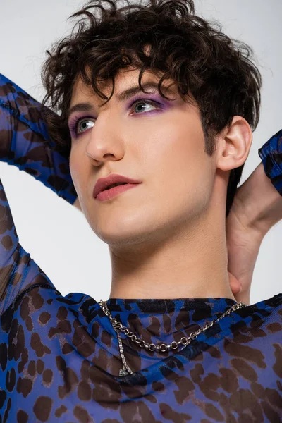 Portrait of young queer person with makeup posing with hands behind head isolated on grey — Stock Photo