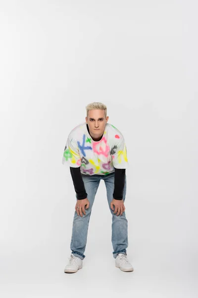 Full length of blonde gay man in trendy clothes looking at camera on grey background — стоковое фото