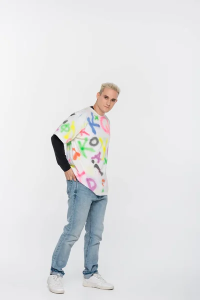 Young and stylish gay man posing with hand in back pocket on grey background — Fotografia de Stock