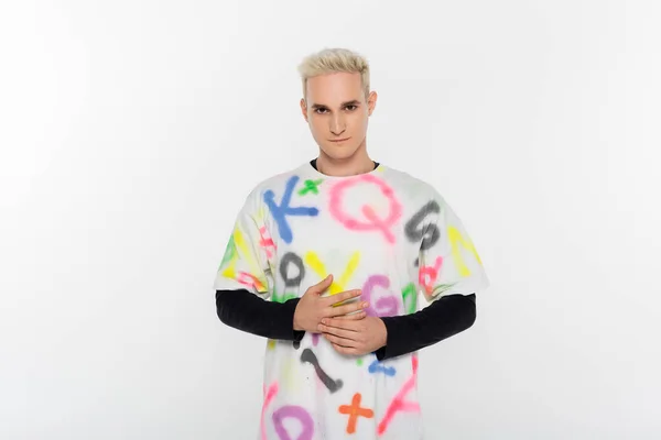 Молодий гей у футболці з принтом алфавіту дивиться на камеру ізольовано на сірому — стокове фото