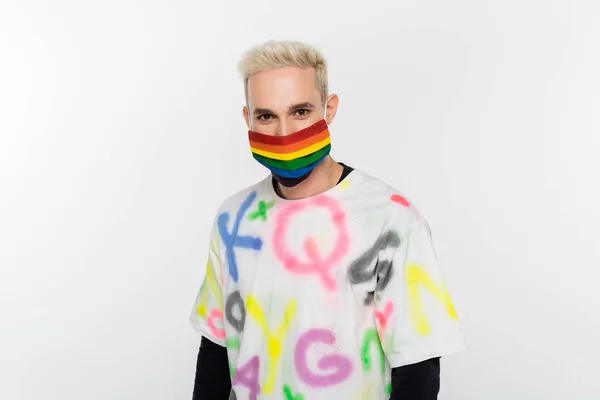 Blonde gay man in trendy t-shirt and lgbtq colors medical mask looking at camera isolated on grey — Stock Photo