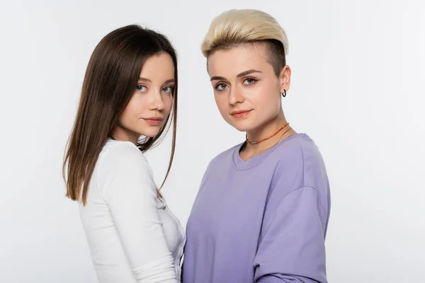 Brunette and blonde lesbian couple with makeup looking at camera isolated on grey — Foto stock