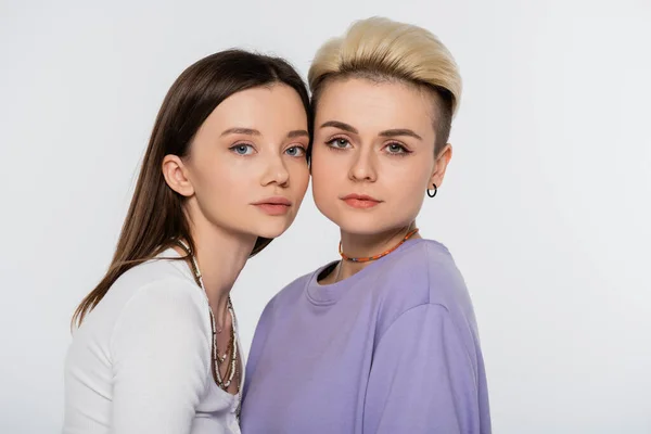 Young and pretty lesbian couple  with beads and makeup looking at camera isolated on grey — Stock Photo