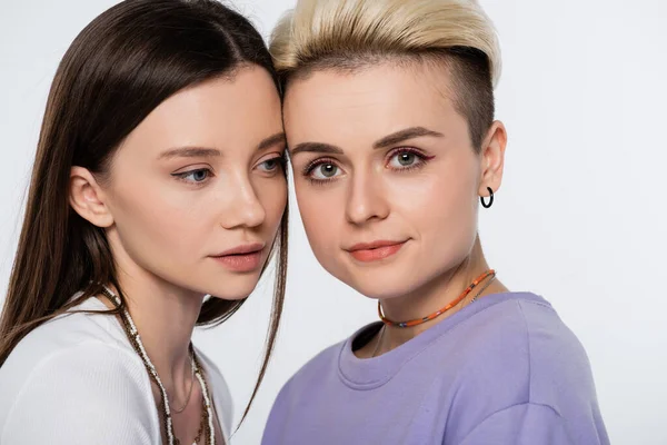 Blonde lesbian woman looking at camera near young brunette girlfriend isolated on grey — Stock Photo