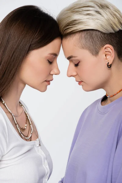 Side view of young lesbian couple with closed eyes standing face to face isolated on grey — Stockfoto