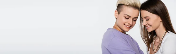 Pretty and trendy lesbian couple with makeup smiling isolated on grey, banner — Stock Photo