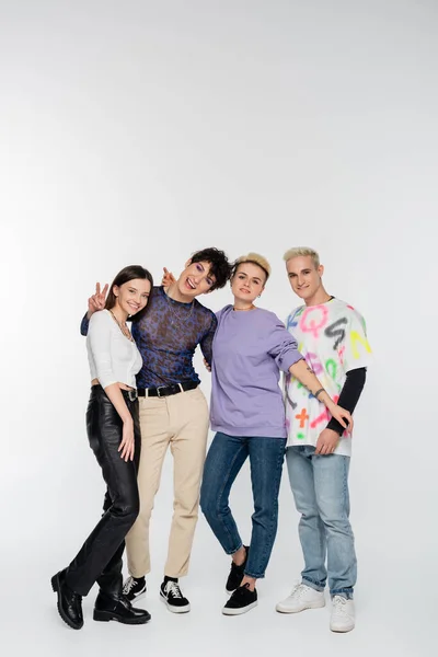 Happy queer person showing victory sign near diverse lgbtq friends on grey background — Stock Photo