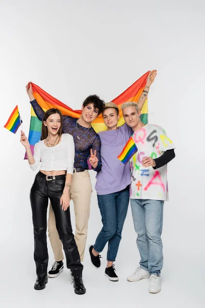 Cheerful friends of diverse identity standing with lgbtq flags on grey background — Stock Photo