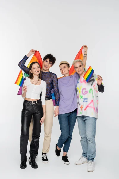 Full length of joyful friends of diverse identity holding lgbtq flags on grey background — стоковое фото