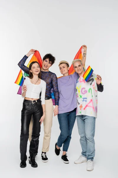 Full length of joyful friends of diverse identity holding lgbtq flags on grey background — Stock Photo