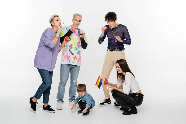 Lgbtq community friends blowing soap bubbles near toddler child on grey background — Foto stock