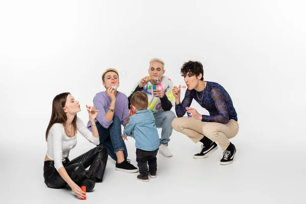 Toddler boy near stylish lgbtq community people blowing soap bubbles on grey background — Stockfoto