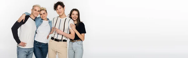 Happy and stylish friends embracing and looking at camera isolated on grey, banner — Photo de stock