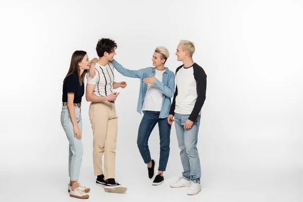 Full length of stylish and cheerful friends gesturing during conversation on grey background — Stock Photo