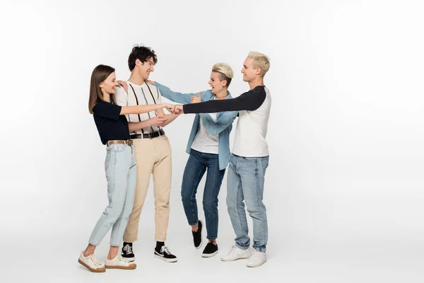 Full length of young friends doing fist bump and showing thumb up on grey background — Stock Photo