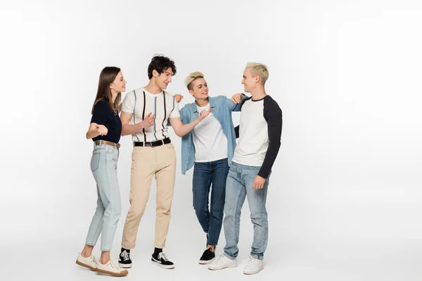 Trendy man pointing with finger while talking to smiling friends on grey background — Photo de stock