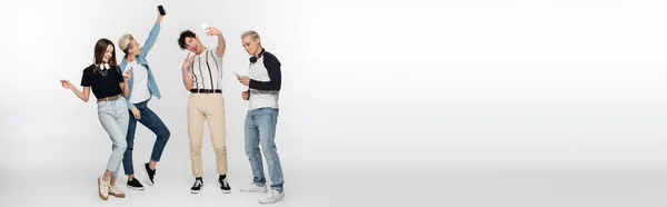 Happy friends taking selfie on mobile phones and dancing on grey background, banner — Stock Photo