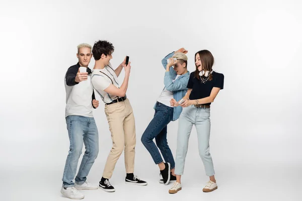 Young men taking photo on smartphones near cheerful women dancing on grey background — Stockfoto