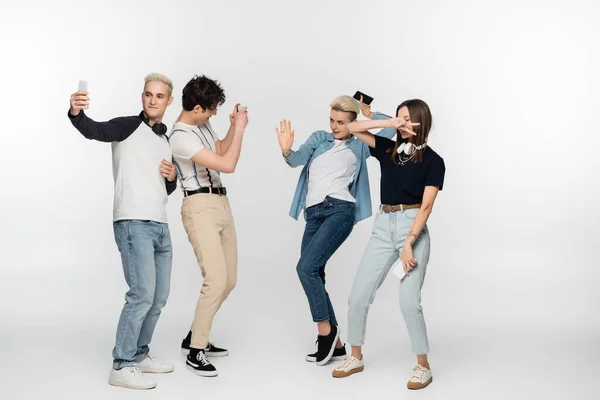 Full length of man taking photo of joyful friends dancing on grey background - foto de stock