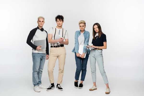 Full length of young friends with laptops and digital tablets on grey background — Stock Photo