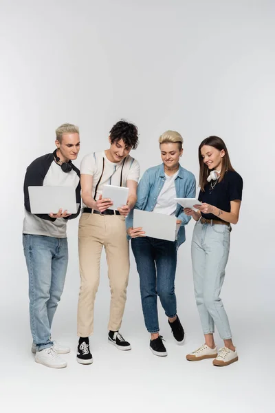 Full length of stylish friends using laptops and digital tablets on grey background — Fotografia de Stock