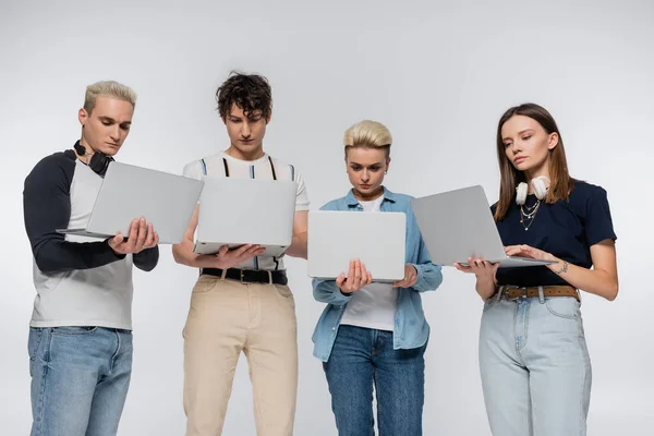 Young freelancers in trendy clothes using laptops isolated on grey — Stock Photo