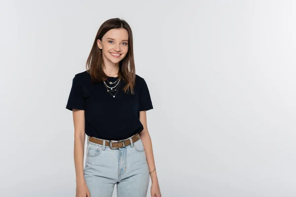 Pretty and happy woman in black t-shirt and jeans smiling at camera isolated on grey - foto de stock