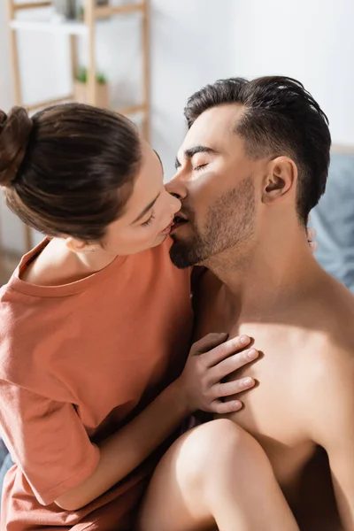 Junge Frau im T-Shirt küsst Freund zu Hause mit geschlossenen Augen — Stockfoto