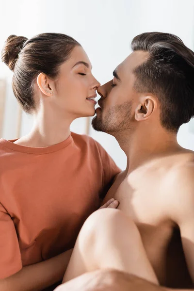 Seductora mujer en camiseta besándose hombre con los ojos cerrados en casa - foto de stock